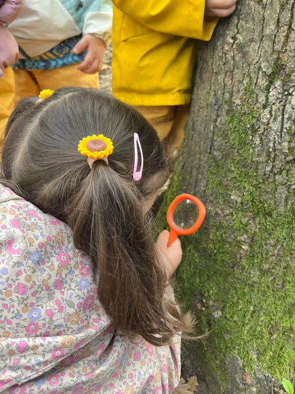 Büyüteçle bir meşe gövdesindeki yosunu inceleyen çocuk, arkadan